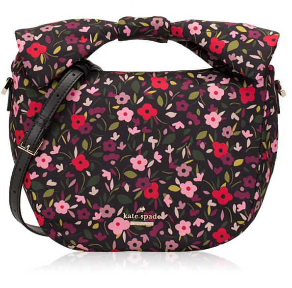 black vinyl bag with rose, purple and pink flowers printed all over it in a satchel style, plus there's a large decorative bow on the top of the handle