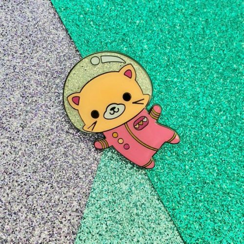Space Kitty enamel pin. A light brown cat in a pink space suit. Its helmet is glittery.