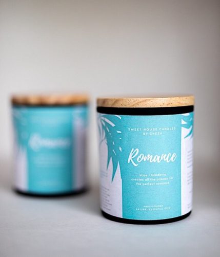 A candle in a dark glass jar with a wooden lid. The label is teal and white.