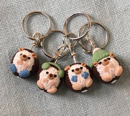 Four stitch markers that are little hedgehogs dressed up in winter gear