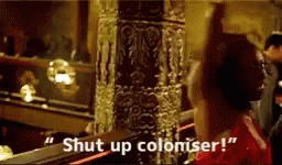 Okoye, from Black panther, flinging a wig at a white due, with the caption SHUT UP COLONIZER.