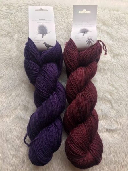 The skeins of yarn side by side against a white background. The skein on the left is a deep purple. The skein on the right is burgundy red.