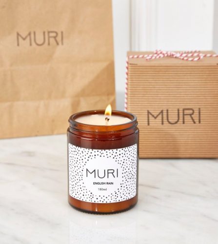 A white candle in a dark amber jar in front of brown paper bags.