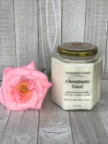 A candle in a hexagonal glass jar beside a pink rose.