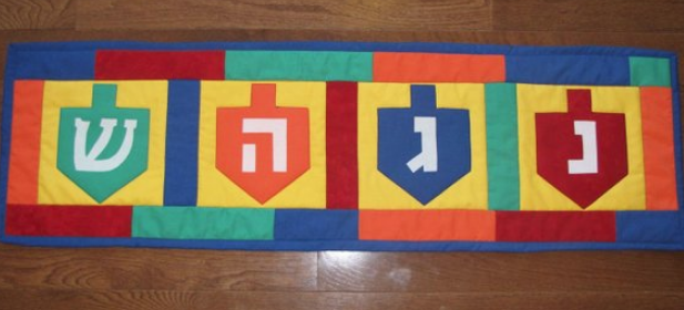 Hanukkah Dreidel table runner in green blue orange an red with four dreidels across the top