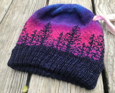Another version of the Alaska hat with a dark blue brim and trees and a pink and violet background.