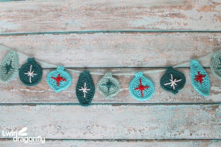 A garland of crocheted Christmas ornaments in teals with red and white accents.