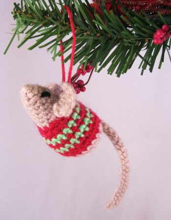 A tiny mouse wearing a red and green sweater hangs from a Christmas tree. And OMG is it cute.