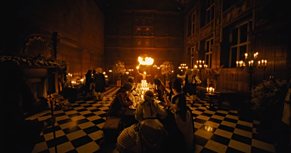 A group of people at dinner, lighted only by candles and a fire breather.