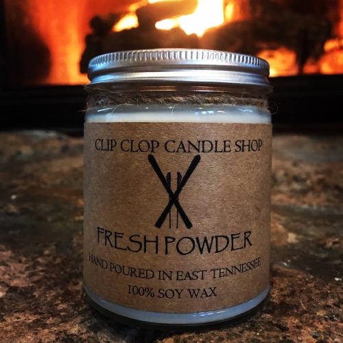 A white candle in a glass jar before a fireplace.