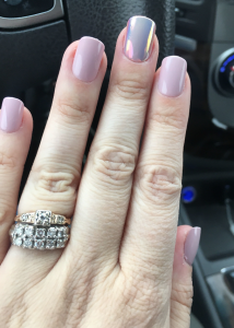 Elyse's press on manicure with four light pink nails and a long middle finger nail that's chrome pink 