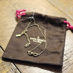 Kate Spade gold plated necklace with mini eyeglasses charm sitting on a brown fabric bag printed with the kate spade logo