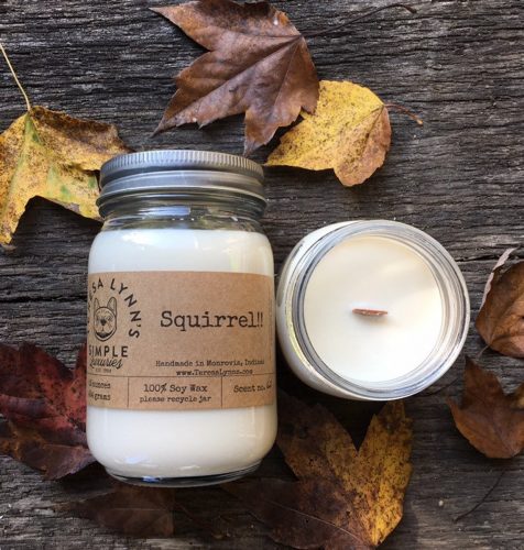 A white candle in a glass mason jar amidst a pile of autumn leaves