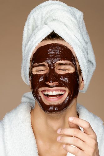 Laughing man with chocolate facial mask.
