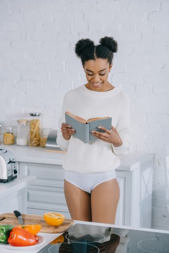 happy young woman reading book at kitchen in morning