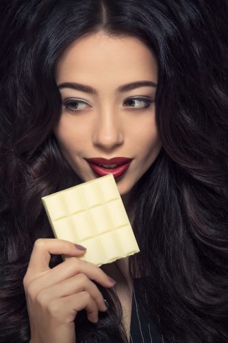 Portrait of professional fashion or vogue model lady holding a bar of white chocolate in front of her while posing for photographer.