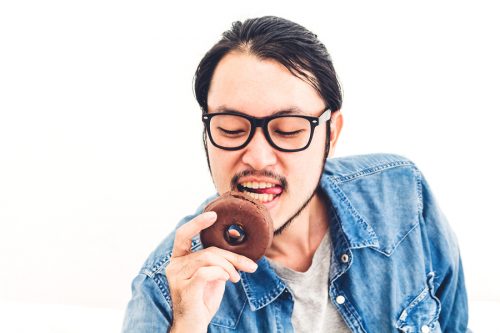 Young Asian man eating a chocolate donut cake at home.