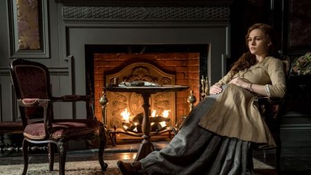 Bree reclines in a chair in front of a fireplace. She looks pensive.