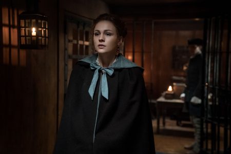 Bree walks through the jail wearing a really beautiful cape tied with a blue ribbon.