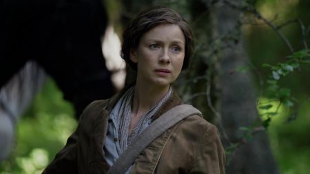 Claire against a forest background. Her horse is standing behind her. She looks worried.