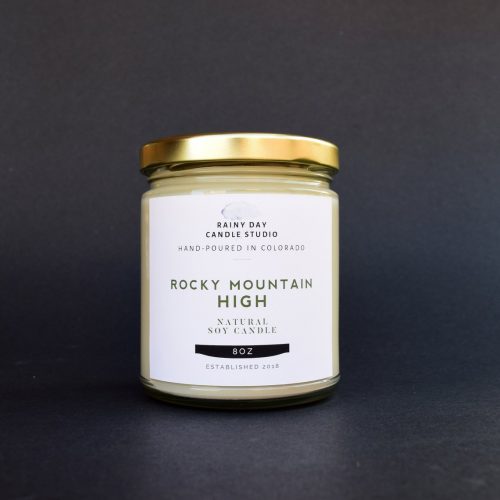 A candle in a glass jar with a gold metal lid against a slate gray background.