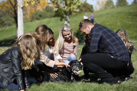 Colton and the woman crouch on the ground, petting Sniper a black lab with a gray muzzle