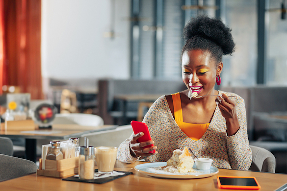 Woman with bright makeup eating dessert and reading message on phone