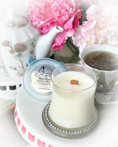 An hourglass jar with a white candle. In the background are some peonies and a fresh cup of tea.