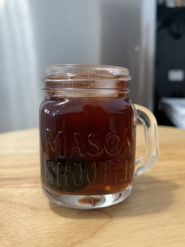 A dark red amber colored cocktail in a mason jar