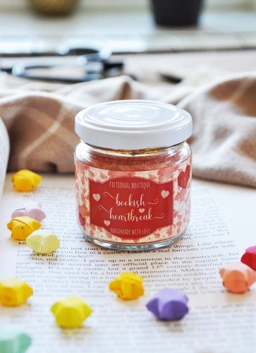 A red candle in a small jar. It's sitting on a book surrounded my origami paper stars.