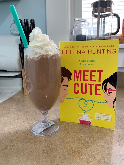 A chocolate peanut butter milkshake next to a copy of Meet Cute by Helena Hunting