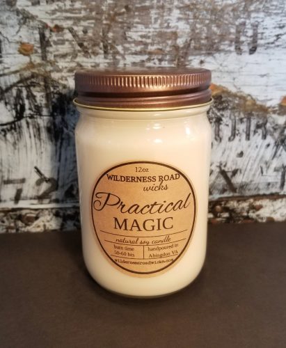 An off white candle in a tall glass jar in front of a white birch background.