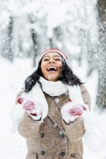 Attractive African American woman throwing snow and smiling in winter forest