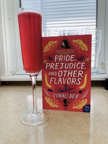 A purplish red drink in a fluted glass next to a copy of Pride, Prejudice, & Other Flavors by Sonali Dev