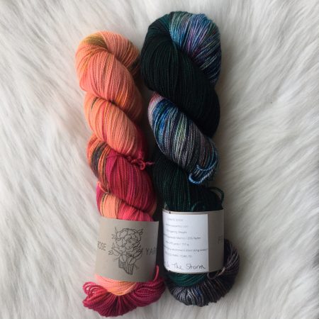 Two skeins of yarn side by side on a white background. The skein on the left is a bright orange with neon pink varigation. The skein the right is a ultra-dark green with marine blue and red and pink varigation.