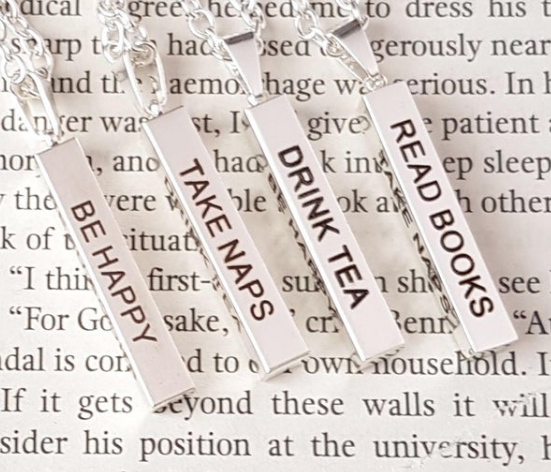 A silver bar pendant that reads on each side read Books, drink tea, take naps, be happy