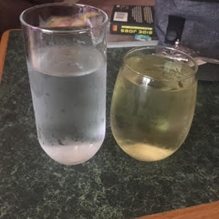 An enitrely full to the brim glass of white wine on the right and a glass of water on the left