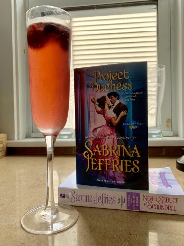A pink sangria with fruit in a fluted glass next to a stack of books.