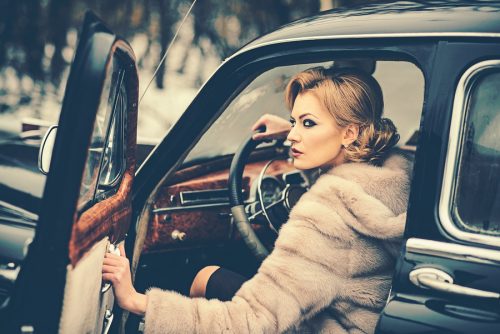 Gorgeous woman in fur coat, sitting behind the wheel of a vintage car.