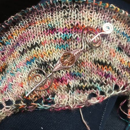 A close up of a multi colored shawl with a jeweled shawl pin