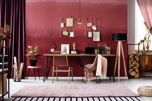 Pink blanket on metal chair next to wooden table in cherry home office interior with plant on stool