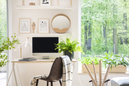 Wooden chair at desk with lamp and desktop computer in home office interior with plants.