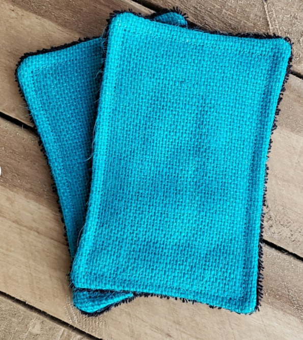 A blue burlap sponge that's machine washable with a black fluffy scrub part on the other side 