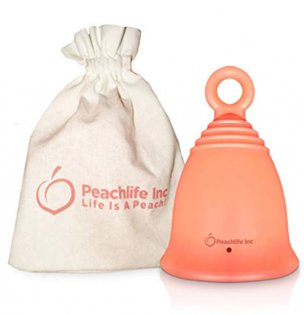 A peach dome shaped menstrual . cup with a loop at the end and a fabric bag for carrying