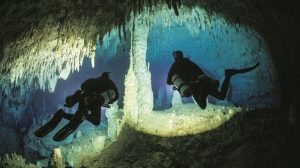 two divers going through cave surrounds by crystal stalagmites and stalactites