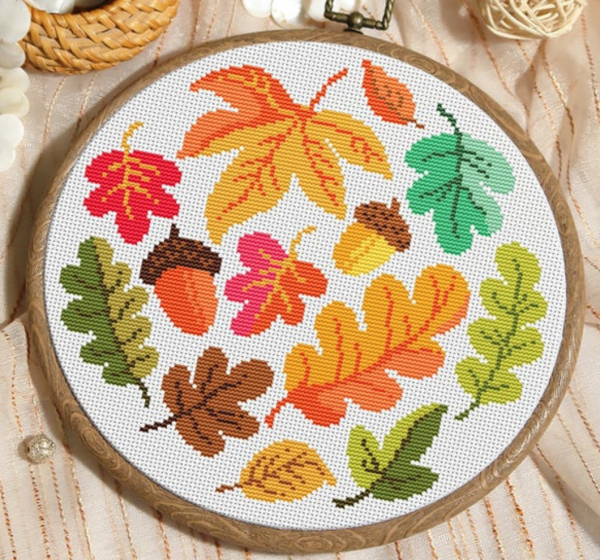 Fall pattern for cross stitch f eaturing green gold red and orange leaves an two acorns arranged in a circular pattern