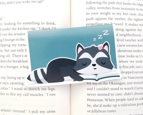 A blue magnetic bookmark with a cute sleepy raccoon on it.