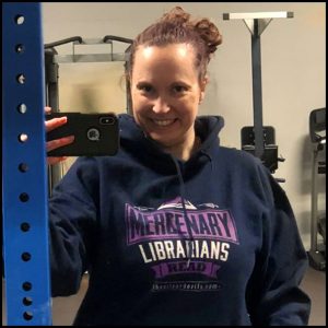 JenniferRNN in a gym by a weight stack wearing a MERCENARY LIBRARIANS READ hooded sweatshirt
