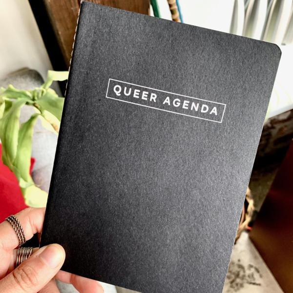 Grey stitched notebook with the words QUEER AGENDA in silver
