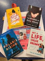 A picture of The Bride Test, Polaris Rising, Get a Life Chloe Brown, an Widow of Rose House on top of a printed tote bag and with a set of four button magnets on a blue countertop